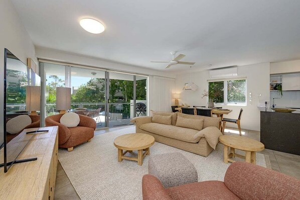 A modern living room with a sofa, two round tables, a ceiling fan, and a kitchen area with a counter and cabinets.