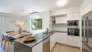 A modern kitchen with white cabinetry, a large island, stainless steel appliances, and a view of greenery outside.