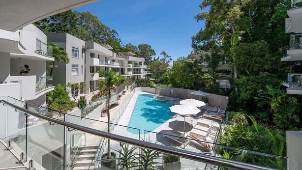 A modern building with a swimming pool, balconies, and lush greenery.