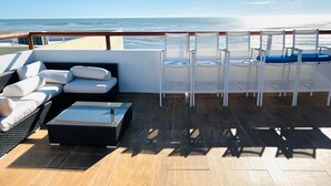 Une terrasse ensoleillée avec un canapé, des fauteuils et une table, d’où l’on a une vue sur l’océan.