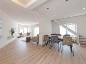 Uma sala de estar ampla com escada moderna, mesa de jantar com cadeiras e uma grande janela que oferece luz natural.