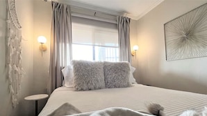 A neatly made bed with fluffy pillows, a bedside table, and a wall-mounted light fixture.