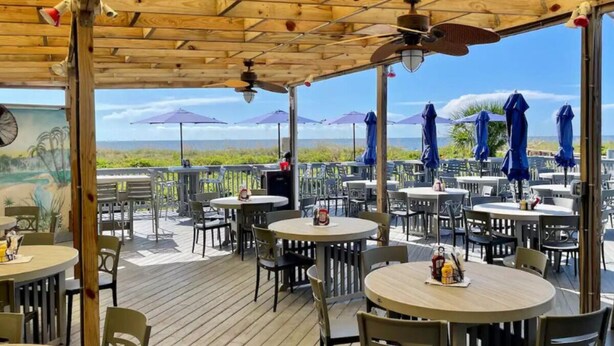 An outdoor patio with round tables and chairs, umbrellas, and a view of the beach.