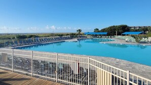 A large outdoor swimming pool with multiple lanes, surrounded by lounge chairs and umbrellas, and a wooden deck in the foreground.