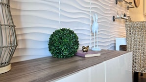 A modern reception area with a textured wall, a wooden reception desk, a green spherical plant, a white sculpture, and a woven chair.
