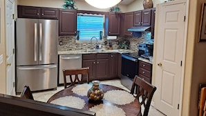 A modern kitchen with dark wooden cabinets, stainless steel appliances, and a central island with a vase. - Cozy Dream Cottage (Colorado Springs)