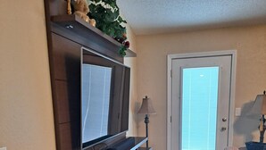 A living room with a TV, two patterned chairs, a bench, a lamp, and a door with blinds. - Cozy Dream Cottage (Colorado Springs)