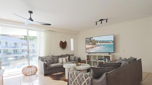 Una sala de estar moderna con un sofá gris, una mesa de centro y un televisor que muestra una escena de playa.