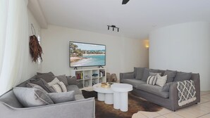 Una sala de estar con dos sofás grises, una mesa de centro blanca y un televisor que muestra una escena de playa.