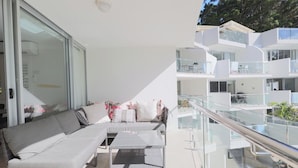 Un espacio exterior moderno con sala, una mesita y barandilla de cristal con vistas a un edificio de varios niveles.