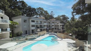 Un hotel moderno con piscina, varios balcones y exuberante vegetación.