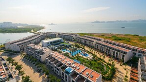 A coastal hotel with multiple buildings, a central pool, and a view of the sea. - Villa 102 Royal Lotus cách bãi biển 5 phút (Hạ Long)