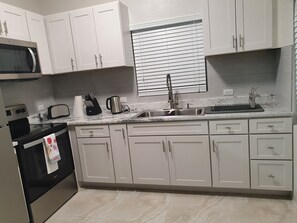 Eine moderne Küche mit weißen Schränken, einer eingebauten Mikrowelle, einem Toaster, einem Wasserkocher und einem Spülbecken mit Wasserhahn.