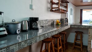 Eine Küche mit modernem Design, inklusive Kaffeemaschine, Toaster und Wasserkocher auf der Arbeitsfläche. Es gibt drei hölzerne Hocker und eine Obstschale auf der Arbeitsplatte.