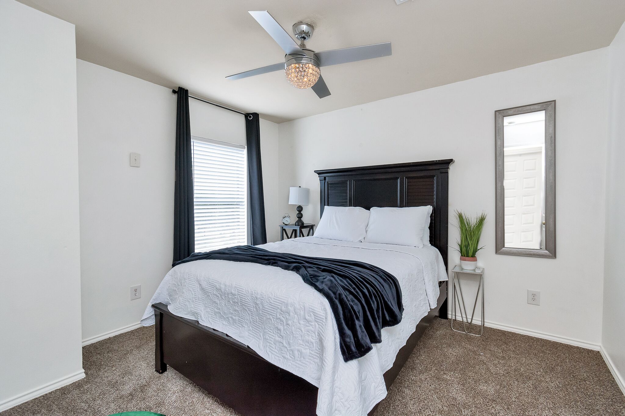Une chambre à coucher avec un lit, un ventilateur de plafond, une table de chevet, une lampe et une fenêtre.