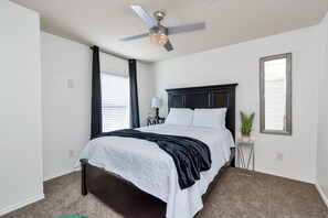 Een slaapkamer met een bed, een plafondventilator, een nachtkastje, een lamp en een raam.