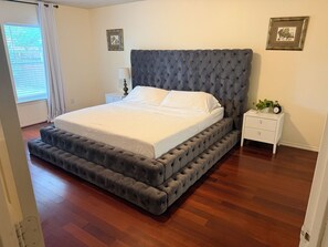 A bedroom with a tufted headboard, a bed with white linens, a nightstand with a lamp, and a small plant.