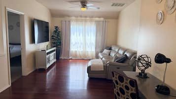 Un salon avec un canapé, un téléviseur, un ventilateur de plafond et une fenêtre avec des rideaux.