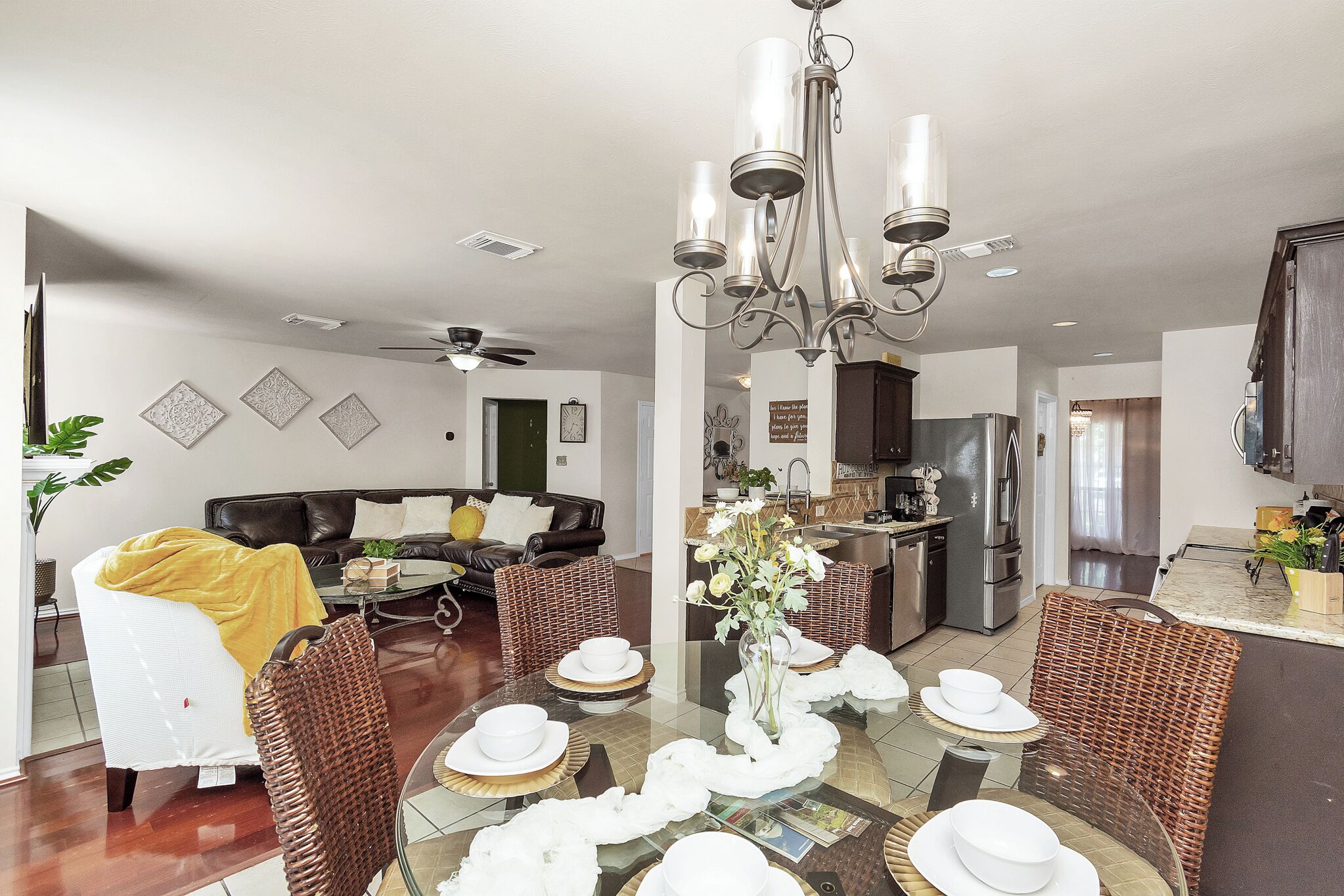 Un salón moderno con una mesa de comedor lista para seis personas, una cocina al fondo y un ventilador de techo.