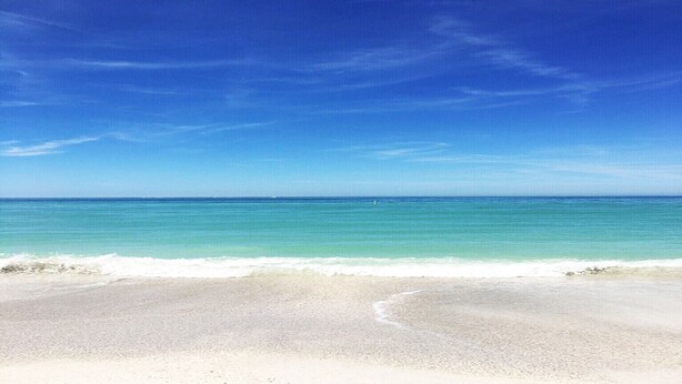 Une plage avec une eau turquoise et limpide et un rivage sablonneux.