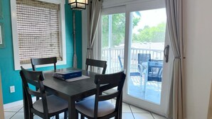 Un coin repas avec une table et des chaises, une fenêtre avec des stores et une vue sur l’extérieur.