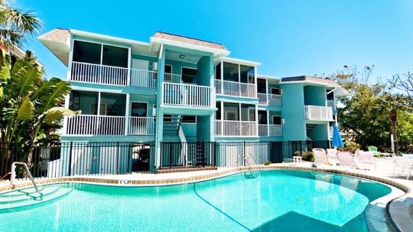 Un hotel de varios pisos con balcones, piscina y entorno tropical.