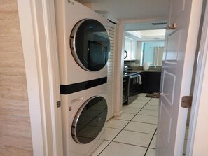 A laundry room with two stacked washing machines, a kitchen area with cabinets and a countertop, and a tiled floor.