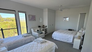 A hotel room with two beds, a desk, a chair, a dresser, and a large window offering a view of the outdoors. - Normanville Beach House - Wake up to the sound of the ocean and bird life. (Normanville)