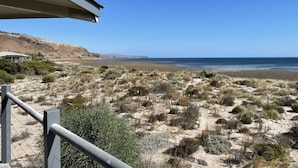 A coastal landscape with a view of the ocean, sandy terrain, and a building with a corrugated roof. - Normanville Beach House - Wake up to the sound of the ocean and bird life. (Normanville)