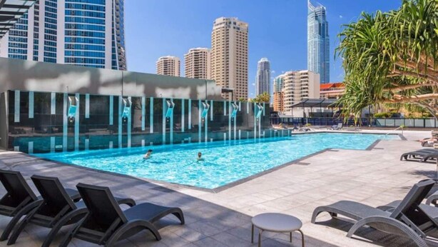Una piscina con sillas de descanso y una mesa, rodeada de edificios altos.