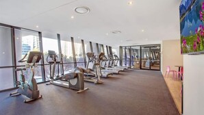Un gimnasio moderno con máquinas de cardio y un amplio ventanal que ofrece vistas a la ciudad.