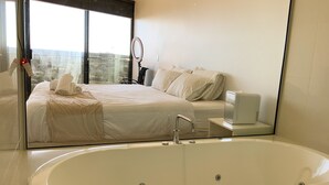 Un dormitorio moderno con una cama grande, una bañera y un espejo amplio.