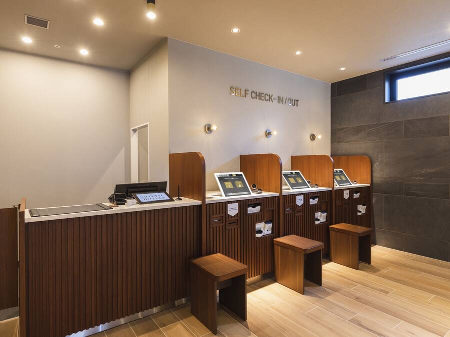 Uma área de check-in e check-out automático, com balcões de madeira e piso ladrilhado.