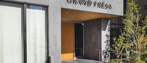 Un edificio moderno con una amplia entrada de vidrio, un letrero que dice "Sofitel Grand Firenze" y un pequeño jardín al aire libre.