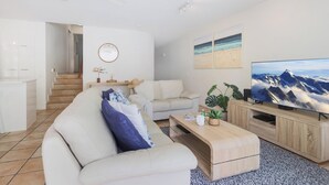 Ein modernes Wohnzimmer mit einer Couch, einem Couchtisch und einem Fernseher. Eine Treppe führt in einen anderen Raum, und an der Wand hängt eine Uhr.