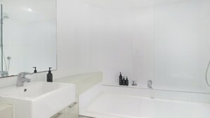 Ein modernes Badezimmer mit einem weißen Waschbecken, einem großen Spiegel und einer Badewanne mit Glaswand.