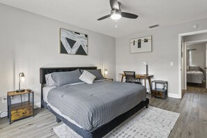 Un dormitorio con cama, mesitas de noche, ventilador de techo y obras de arte en las paredes.