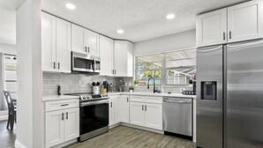 Una cocina moderna con armarios blancos, electrodomésticos de acero inoxidable y un amplio ventanal que proporciona luz natural.