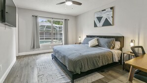 Un dormitorio con cama, escritorio, silla, ventilador de techo, televisor y ventana con cortinas.