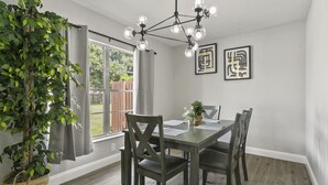 Un comedor con una mesa de madera, sillas oscuras, una lámpara colgante y una planta en maceta.