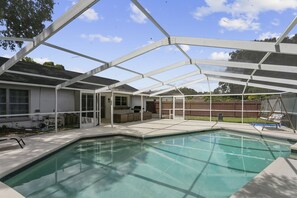 Una piscina cubierta al aire libre con zona de patio, terraza de madera y patio trasero cercado.