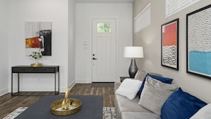 A modern living room with a grey sofa, a black coffee table, and a console table with a plant. - The Oasis - Modern 3BR Near Downtown - Med Center - Stadiums (Houston)
