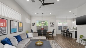 Ein modernes Wohnzimmer mit Sofa, Couchtisch und Kunstwerken an der Wand. Es gibt einen Essbereich mit Tisch und Stühlen sowie eine Küche mit Fernseher und Arbeitsfläche.