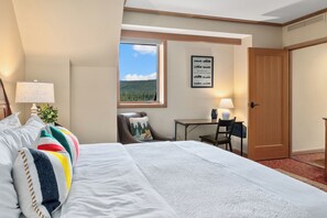 Habitación de hotel con una cama grande, un escritorio, una silla, una ventana con vistas a un bosque y una puerta.