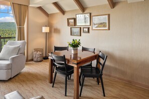 Un comedor con una mesa de madera, cuatro sillas, un jarrón con flores y cuadros en la pared.