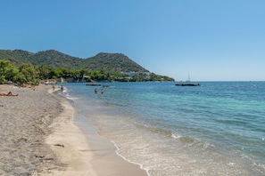 A beach with clear water, a sandy shore, and a mountain in the background.