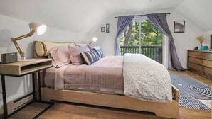 Une chambre moderne avec un lit en bois, un bureau doté d’une lampe et une vue sur la verdure à l’extérieur.