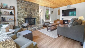 Un salon chaleureux avec une cheminée en pierre, un plafond en bois et un téléviseur à écran plat.