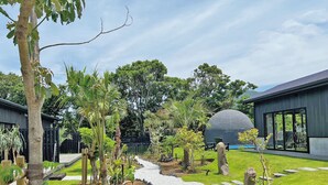 A garden pathway leading to a modern building with a dome structure. - LAVA SAUNA & VILLA (Hachijo)