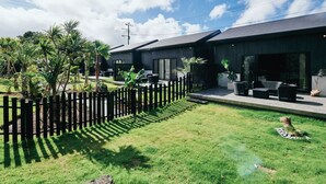 A modern building with a flat roof, a wooden fence, and a grassy lawn. - LAVA SAUNA & VILLA (Hachijo)